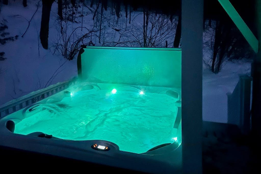 Hot tub lit teal beside the tree line at night